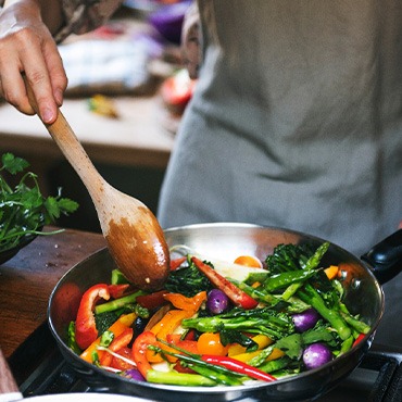 Someone stirring sauteed vegetables with a wooden spoon