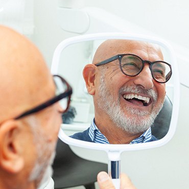 Back of man’s bald head and his smiling face reflected in handheld mirror