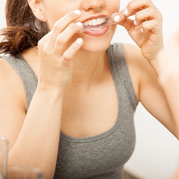 Woman putting on teeth whitening strip at home