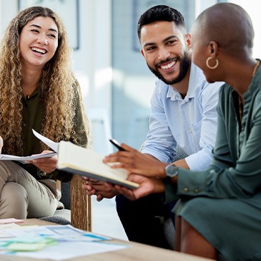 Three adults discussing work project at table with notebooks and printouts