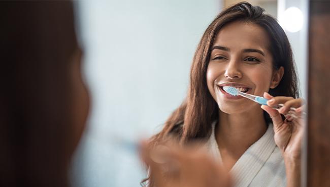 woman brushing teeth in mirror