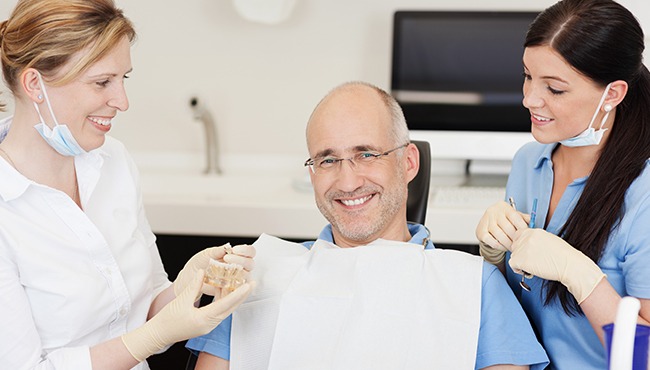 man smiling in chair and two members smiling