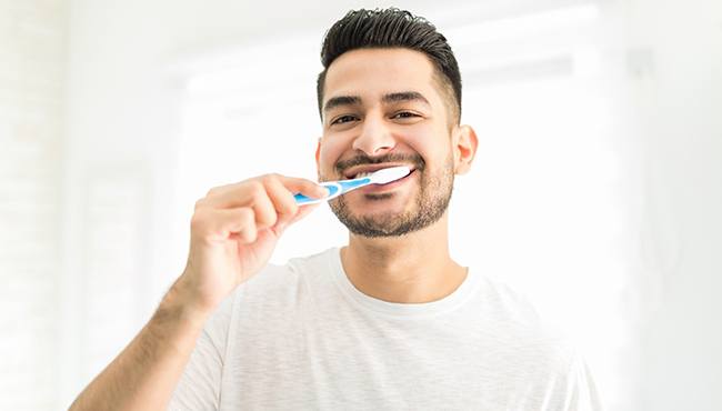 man smiling while brushing teeth in bathroom mirror 