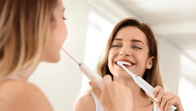 woman brushing teeth with electric toothbrush