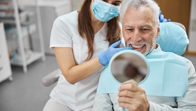 An older man admiring his new dental implant with a hand mirror