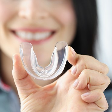 A smiling woman holding a transparent mouthguard in her hand