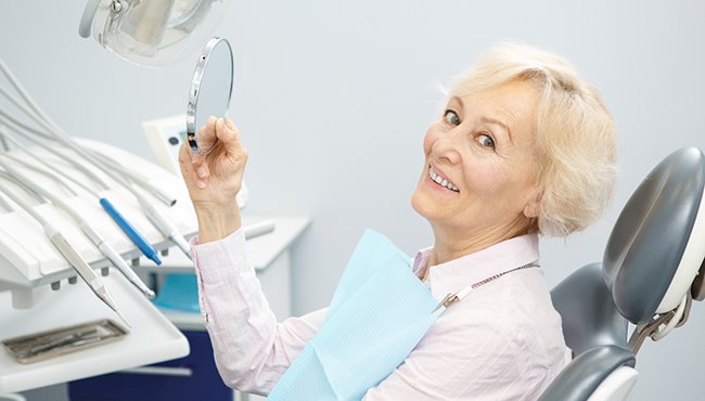 Mature woman using mirror to admire her new implant dentures