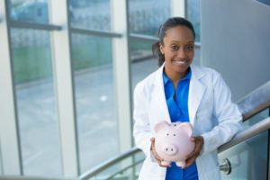 smiling dentist holding pink piggy bank 