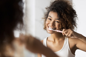 Woman smiling and brushing her teeth in bathroom mirror
