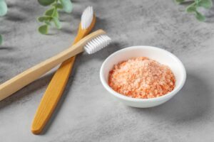 Two wooden toothbrushes on a gray table next to a small dish of Himalayan salt